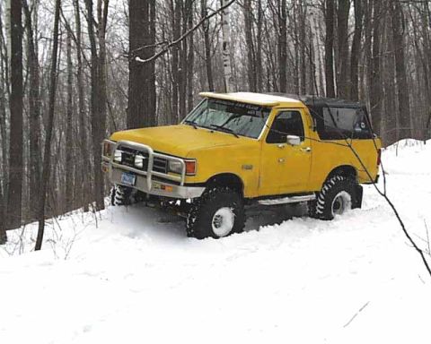1988 Ford Bronco - A yellow 1988 Ford Bronco navigates a snowy forest trail with its off-road tires.