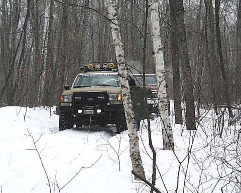 1988 Ford Bronco - Two vehicles navigate a snowy forest path in winter.