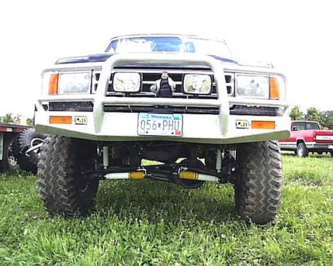 1988 Ford Bronco - Front view of a modified 1988 Ford Bronco, a bull bar and off-road tires. Another truck is visible in the background.