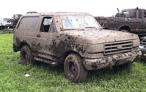 1988 Ford Bronco - A heavily mud-caked 1987 Ford Bronco sits in a grassy field next to another dirty truck.