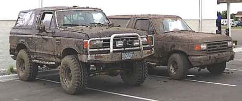 1988 Ford Bronco - Two mud-caked SUVs, including a 1988 Ford Bronco, are parked in a lot after an off-road excursion.