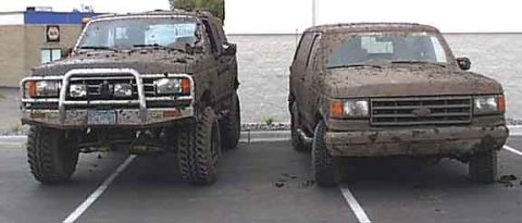 1988 Ford Bronco - Two mud-covered Ford Broncos are parked in a lot after off-roading.