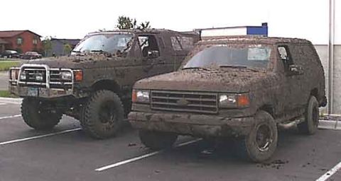 1988 Ford Bronco - Two SUVs are covered in mud after an off-road excursion.