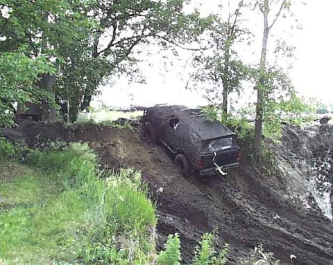 1988 Ford Bronco - A black SUV struggles on a very muddy, steep hill, with trees and greenery surrounding the scene.