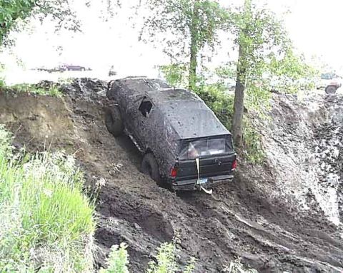 1988 Ford Bronco - A black SUV navigates a steep, muddy incline, with another vehicle visible in the distance.