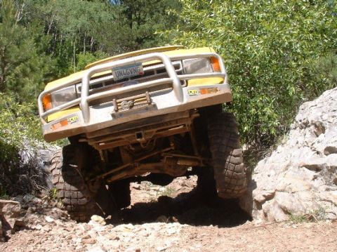 1988 Ford Bronco - Yellow 1988 Ford Bronco navigating a steep, rocky trail with trees in the background.