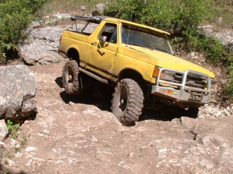 1988 Ford Bronco - This yellow SUV is tackling a challenging rocky terrain with its large off-road tires.