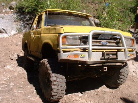 1988 Ford Bronco - This yellow Ford Bronco has a brush guard and large off-road tires, suggesting it is modified for off-road use.