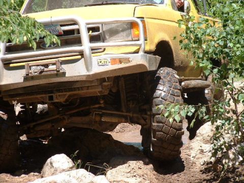 1988 Ford Bronco - This yellow truck is navigating a difficult off-road course with large tires and a winch.