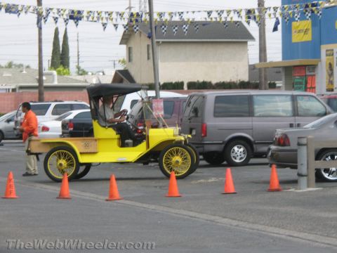 1968 Ford Mustang - An old-fashioned yellow car with a canvas top is parked in a lot with traffic cones and other vehicles.