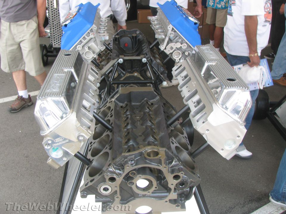 V8 engine block with polished aluminum valve covers and blue intake manifolds, displayed outdoors