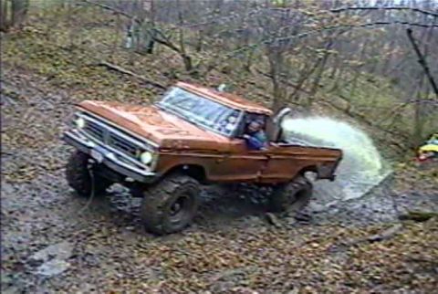 1988 Ford Bronco - Pickup truck navigates a challenging muddy terrain, kicking up a large spray of water.