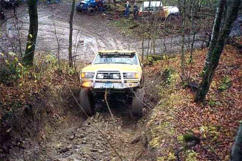 1988 Ford Bronco - A yellow off-road vehicle is being pulled by a winch through a muddy trail, with other vehicles visible in the background.