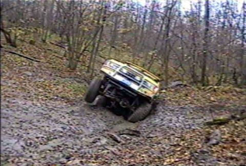 1988 Ford Bronco - This vehicle is navigating a difficult, muddy terrain in a wooded area.