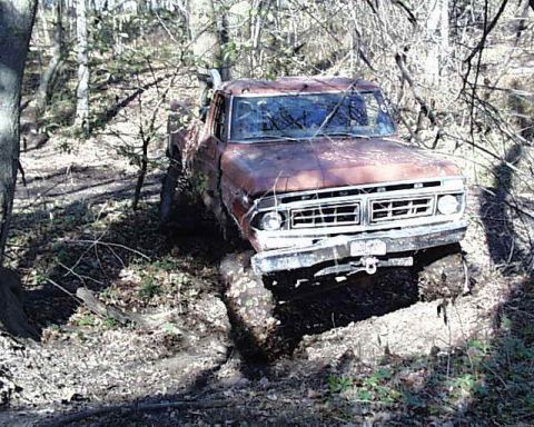 1988 Ford Bronco - This rusty pickup truck appears to be stuck off-road in a wooded area.