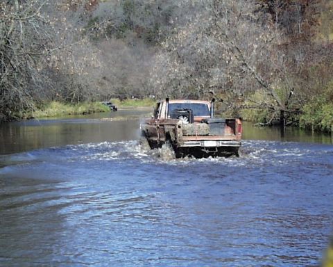 1988 Ford Bronco - A pickup truck navigates a river crossing, with another vehicle in the distance.