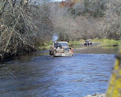 1988 Ford Bronco - Two trucks navigate a waterway during an off-road excursion.