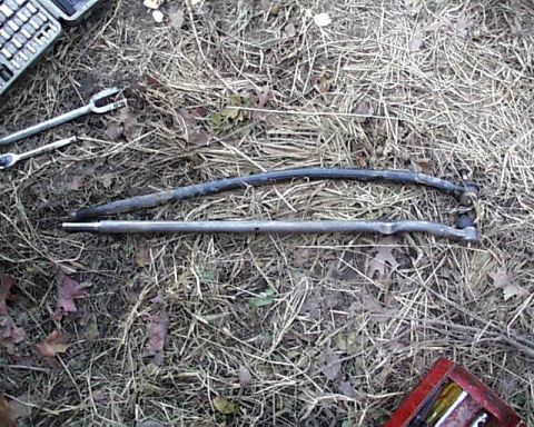 1988 Ford Bronco - Two tie rods and a socket wrench set are lying on the ground amidst dry grass and fallen leaves.