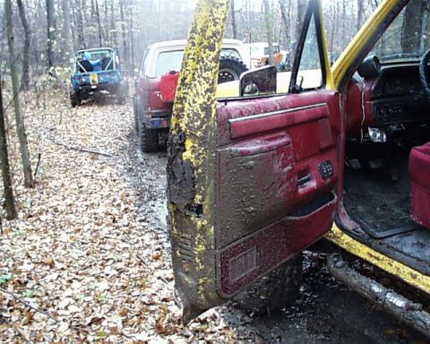 1988 Ford Bronco - Several off-road vehicles are seen on a muddy forest path during an event.