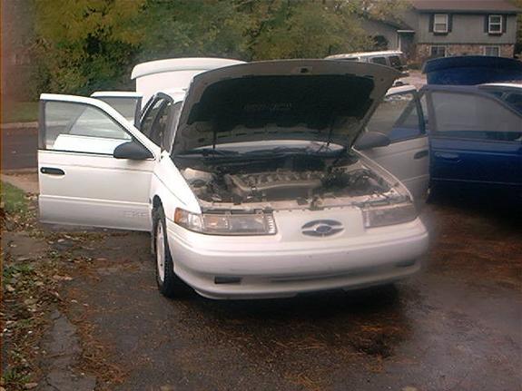 White Ford Taurus sedan with hood and door open in a driveway
