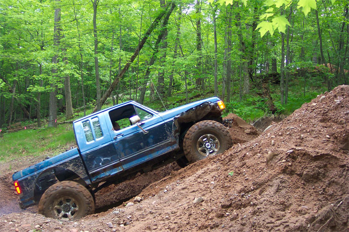 Blue lifted pickup on oversized tires climbing a dirt hill in the woods