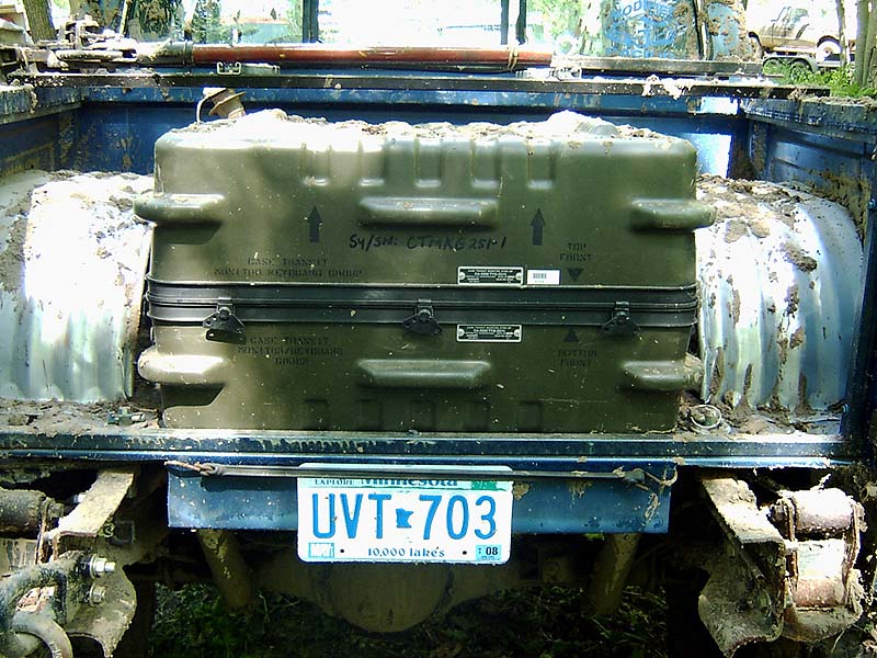 Rear of muddy blue pickup with olive military case and Minnesota plate UVT 703