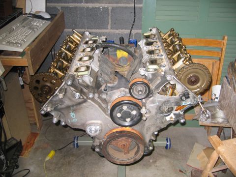 1996 Ford Crown Victoria - Engine assembly with gold valve covers and visible timing gears, resting on a stand.