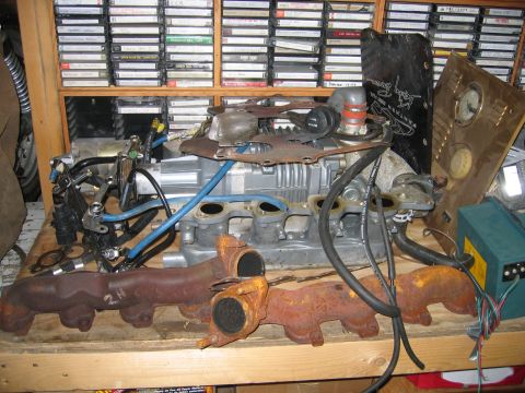 1996 Ford Crown Victoria - Engine components and exhaust manifolds are laid out on a table, with a collection of cassette tapes visible on shelves behind them.