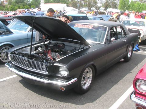 1968 Ford Mustang - A matte black coupe with its hood open, revealing the engine and chrome details at a car show.