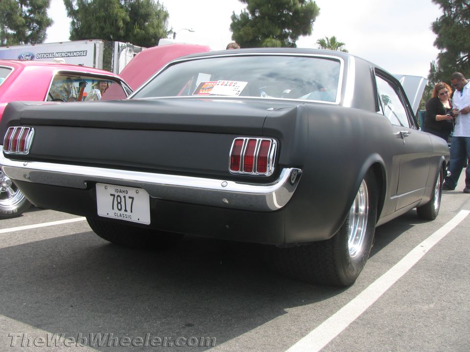 Black 1965 Ford Mustang coupe, rear view, with Idaho license plate 7817. Pink car visible to the left