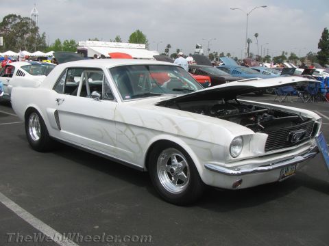 1968 Ford Mustang - A white coupe with flame decals and a roll cage is displayed with its hood open at a car show.