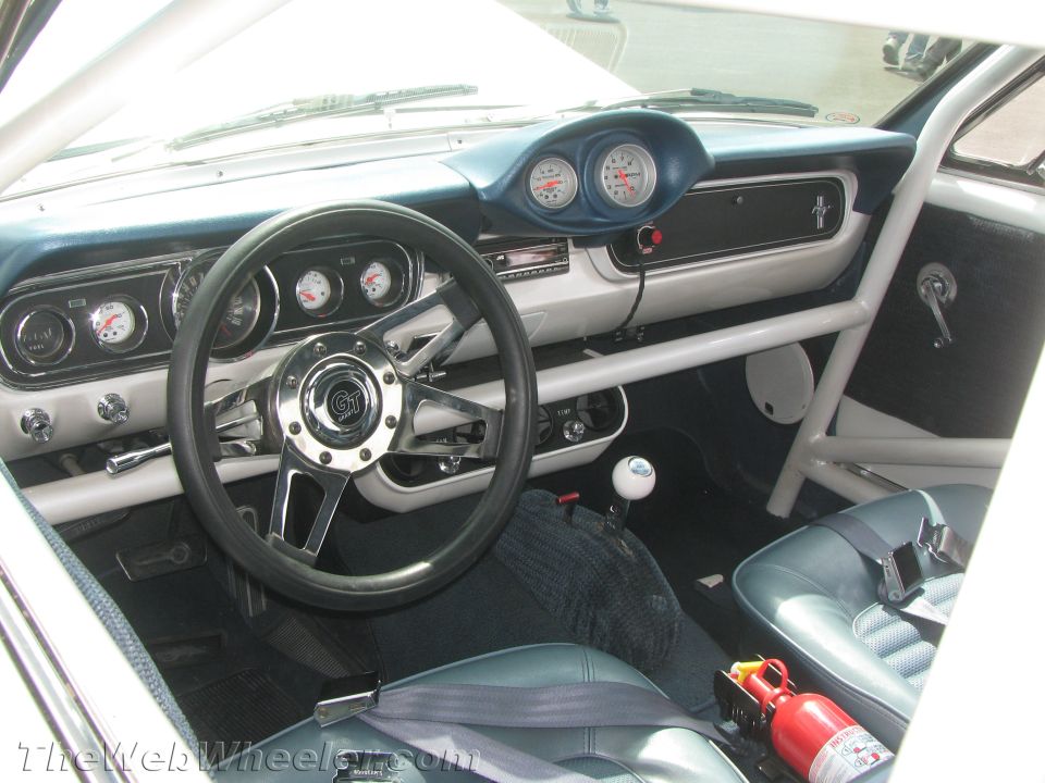 Car interior with racing bucket seats, roll cage, and aftermarket gauges. A fire extinguisher is visible
