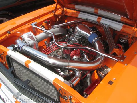 1968 Ford Mustang - The engine bay of an orange 1968 Ford Mustang features a chrome intake system and bright red spark plug wires.