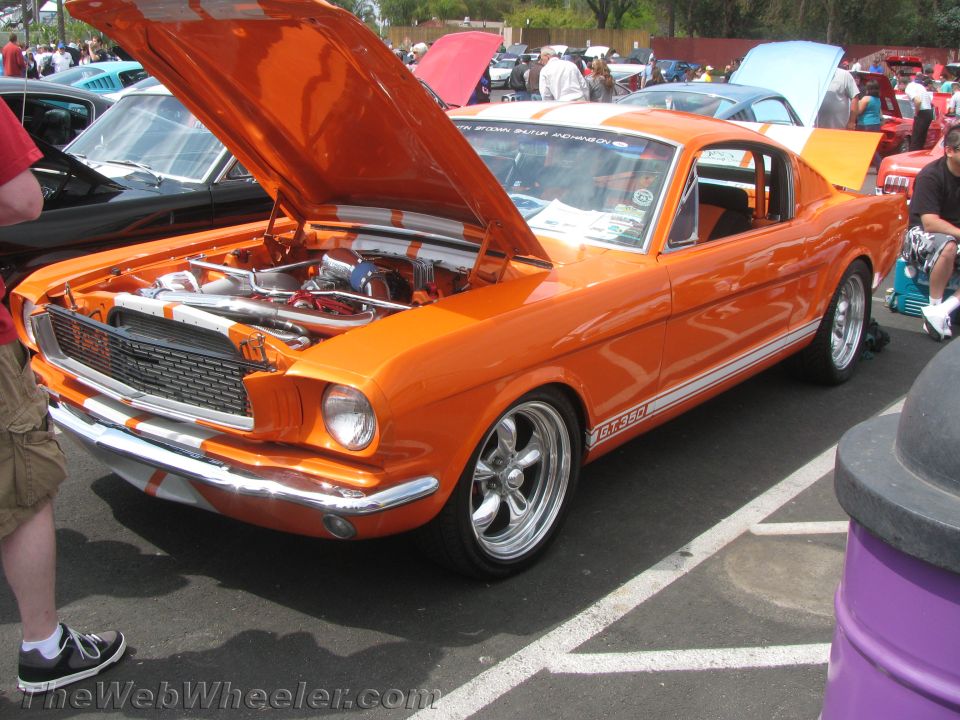 Orange 1965 Ford Mustang GT350 with hood open, showing engine and white racing stripes