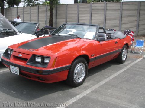 1968 Ford Mustang - This red convertible features a black hood stripe and a "5.0" badge, indicating it is likely a Fox body Mustang from the late 1980s.
