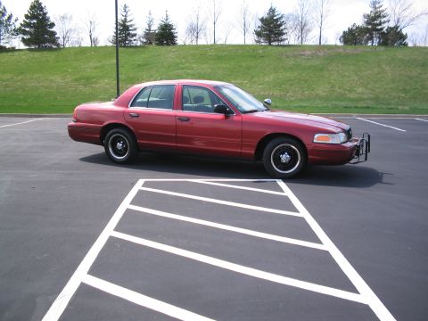 2001 Ford Crown Victoria - A red 2001 Ford Crown Victoria sedan is parked in a lot, showing its side profile and front push bumper.