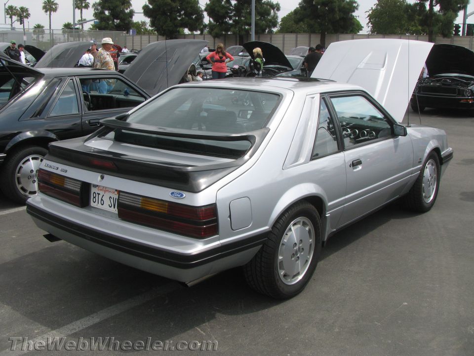 Silver Ford Mustang hatchback with a rear spoiler and California plates BT6 SV. Another black car is parked to its left