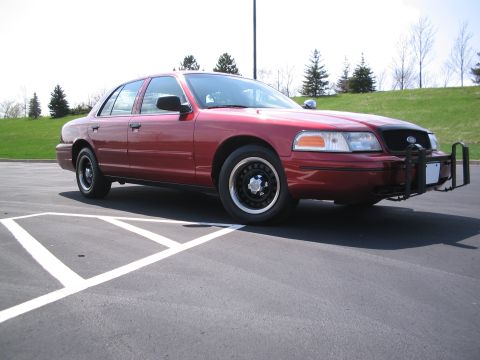 2001 Ford Crown Victoria - A red 2001 Ford Crown Victoria is parked in a lot with a push bumper attached to the front.