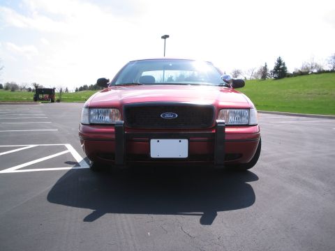 2001 Ford Crown Victoria - A red 2001 Ford Crown Victoria is parked facing forward in a parking lot, equipped with a push bar.