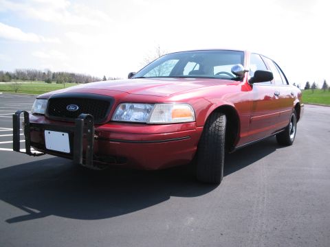 2001 Ford Crown Victoria - A red Ford Crown Victoria, possibly a police car, is shown from the front quarter angle with a push bumper attached.