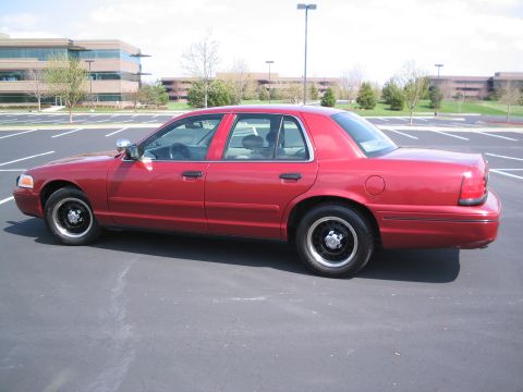 2001 Ford Crown Victoria - A red 2001 Ford Crown Victoria is shown from the side in a parking lot with office buildings in the background.