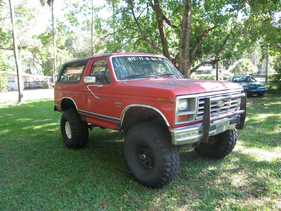 Red Ford Bronco with lifted suspension and large tires parked on grass