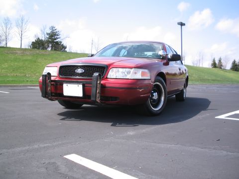 2001 Ford Crown Victoria - A red 2001 Ford Crown Victoria is parked in an asphalt lot with a push bumper attached to the front.