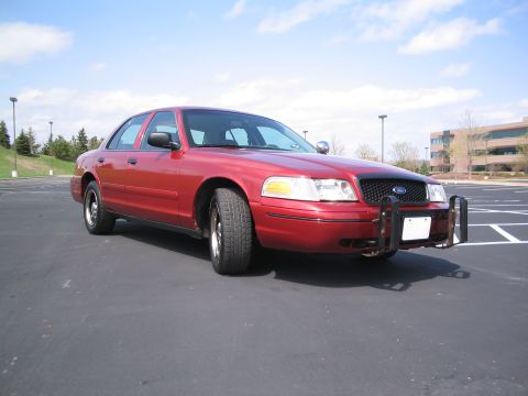 2001 Ford Crown Victoria - This red 2001 Ford Crown Victoria sedan is equipped with a push bar and parked in an asphalt lot.