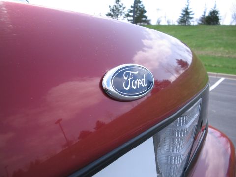 2001 Ford Crown Victoria - Ford emblem on the hood of a red vehicle, with a partial view of the headlight.