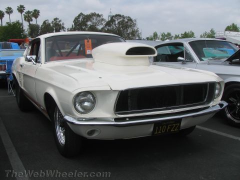 1968 Ford Mustang - A modified 1967 Ford Mustang with a prominent hood scoop is parked at an outdoor car show.