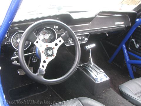 1968 Ford Mustang - The interior of a classic car features a custom steering wheel and a prominent blue roll cage.