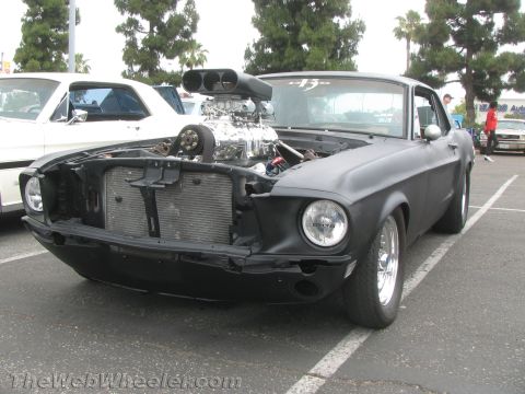 1968 Ford Mustang - A heavily modified 1968 Ford Mustang with a prominent supercharger is parked in a lot next to another vehicle.