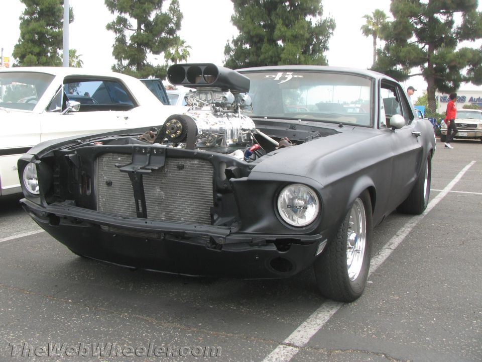 Matte black 1968 Ford Mustang with a large supercharger and hood scoop, viewed from the front