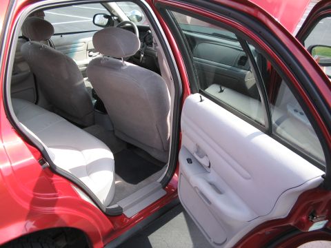 2001 Ford Crown Victoria - The interior of a red sedan is visible with both rear doors and the front passenger door open, revealing the seating area.